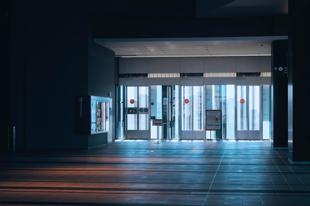 渋谷ヒカリエ11階のエレベーターホール。暗い室内にシースルーエレベーターの大きな窓から青白い光と夕日のようなオレンジ色の光が差し込み、床にコントラストの強いストライプ状の影を作っています。